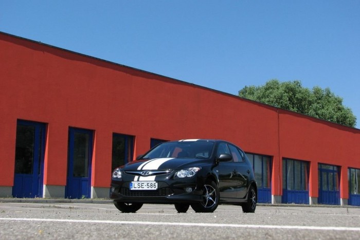 Csíkos Hyundai sötétnarancs épület és kék ég alatt. Nehéz elképzelni giccsesebb látványt