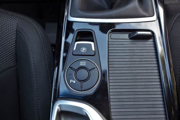 Széria az elektromos kézifék, mögötte a gombcsoport, amelyben középen helyezik el a hátsó szélvédő rolójának nyomógombját