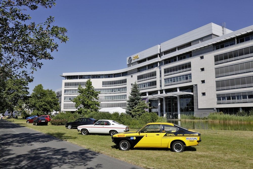 Régi Opelek sorfala a márka rüsselsheimi központja előtt. Előtérben egy Kadett C Coupé, mögötte egy Manta A, amögött egy Kadett E GSi