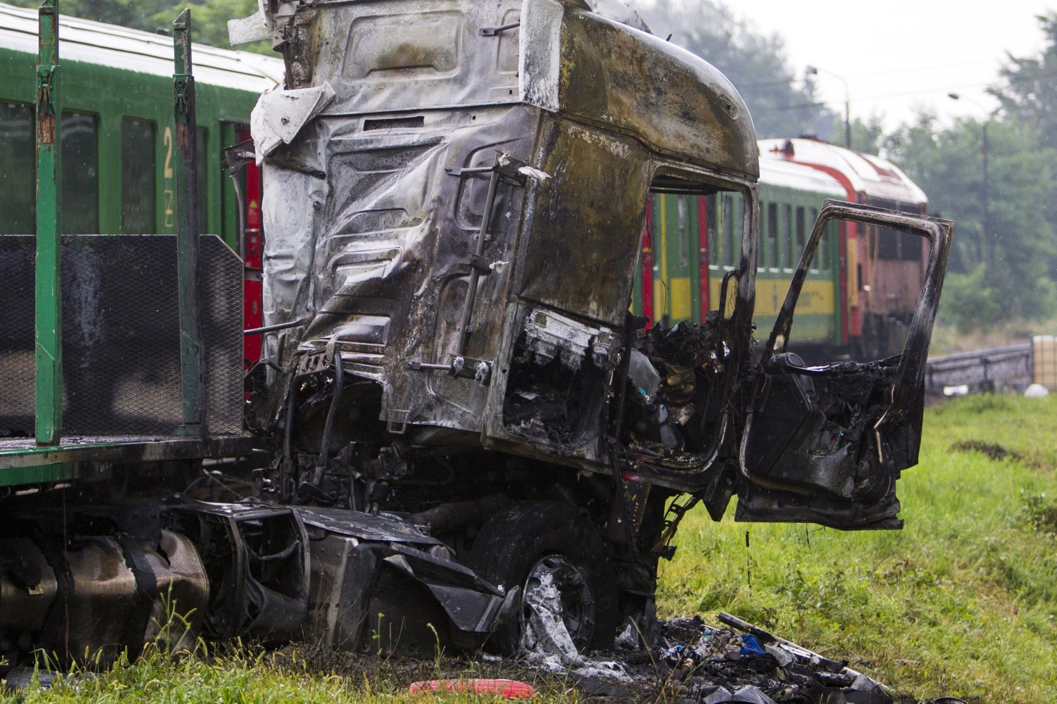 Barcs, 2016. július 25. Összeroncsolódott, kiégett kamion egy személyvonat mellett egy barcsi vasúti átjárónál 2016. július 25-én, miután a két jármû összeütközött. A kamion az ütközés következtében kigyulladt, vezetõje a helyszínen meghalt. A Sopron és Pécs között közlekedõ szerelvény mozdonyvezetõje és egy utasa könnyû sérülést szenvedett. MTI Fotó: Varga György