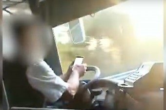Videón a könyökével kormányzó, telefont nyomkodó magyar buszsofőr