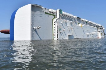 Több ezer autóval a gyomrában borult fel egy óriáshajó